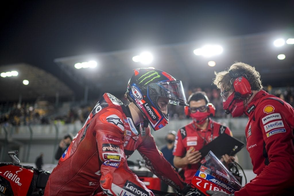 Ducati racer seated on the motorbike in the foreground with team members in the back 