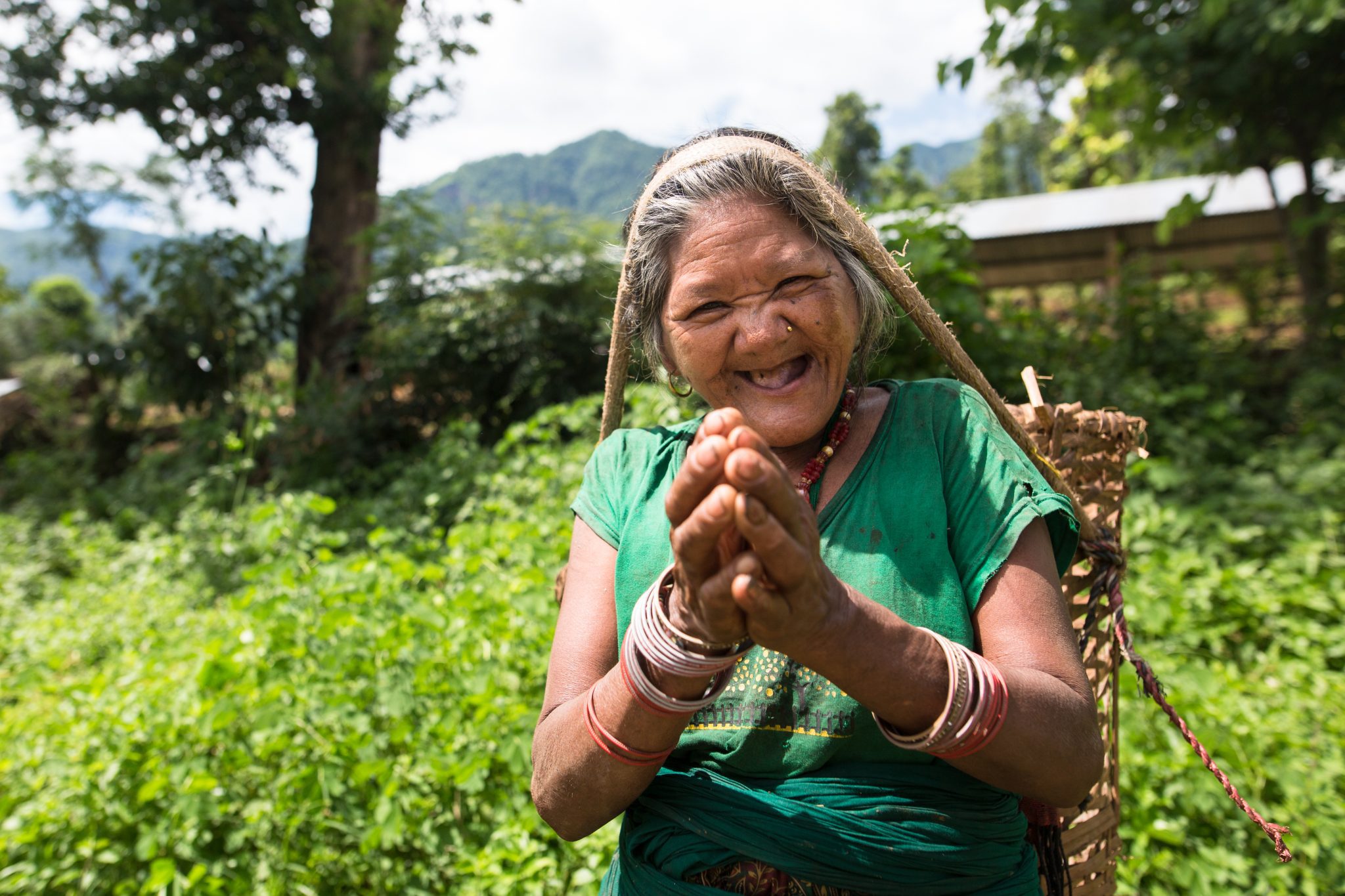 Nepali woman smiling and carrying a basket on her head in Riatole, Nepal